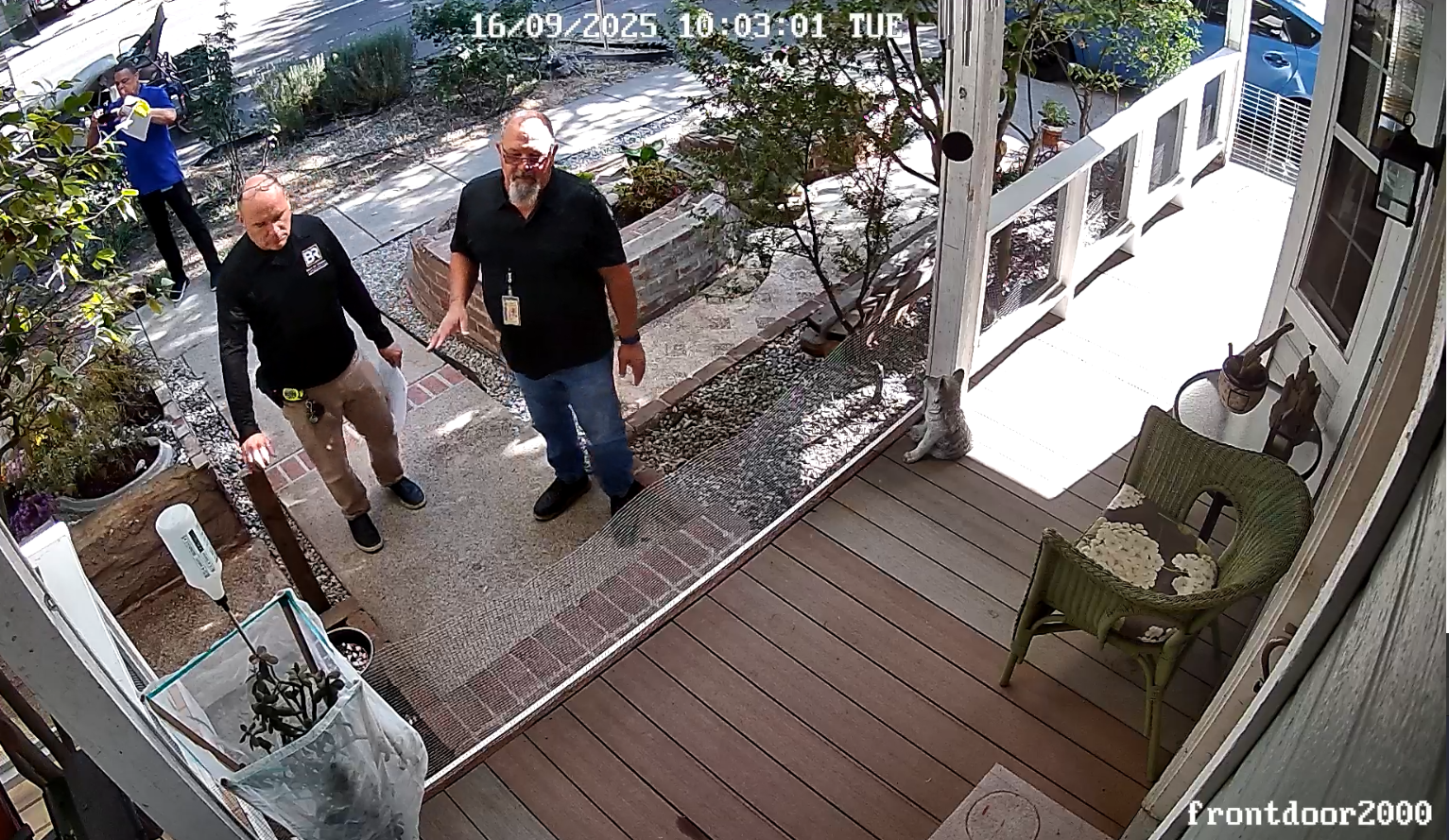 Wide front-door CCTV screenshot at 10:03:01 showing blue-shirt official with phone near the front of the property.